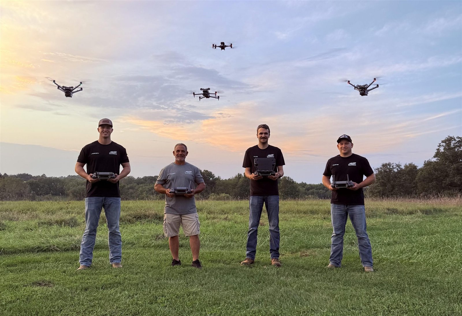 Four Recon1 drone pilots holding controllers with drones flying overhead at sunset
